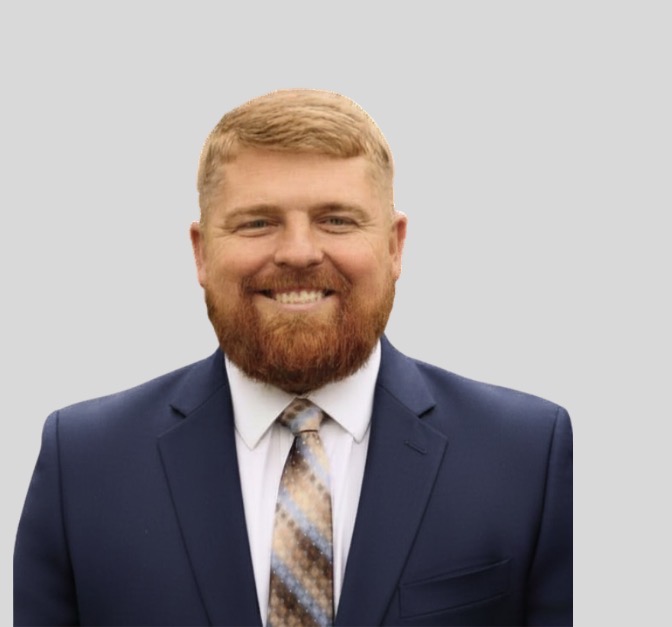Screenshot | The Real Estate Company Smiling man in a navy suit and patterned tie against a light gray background.